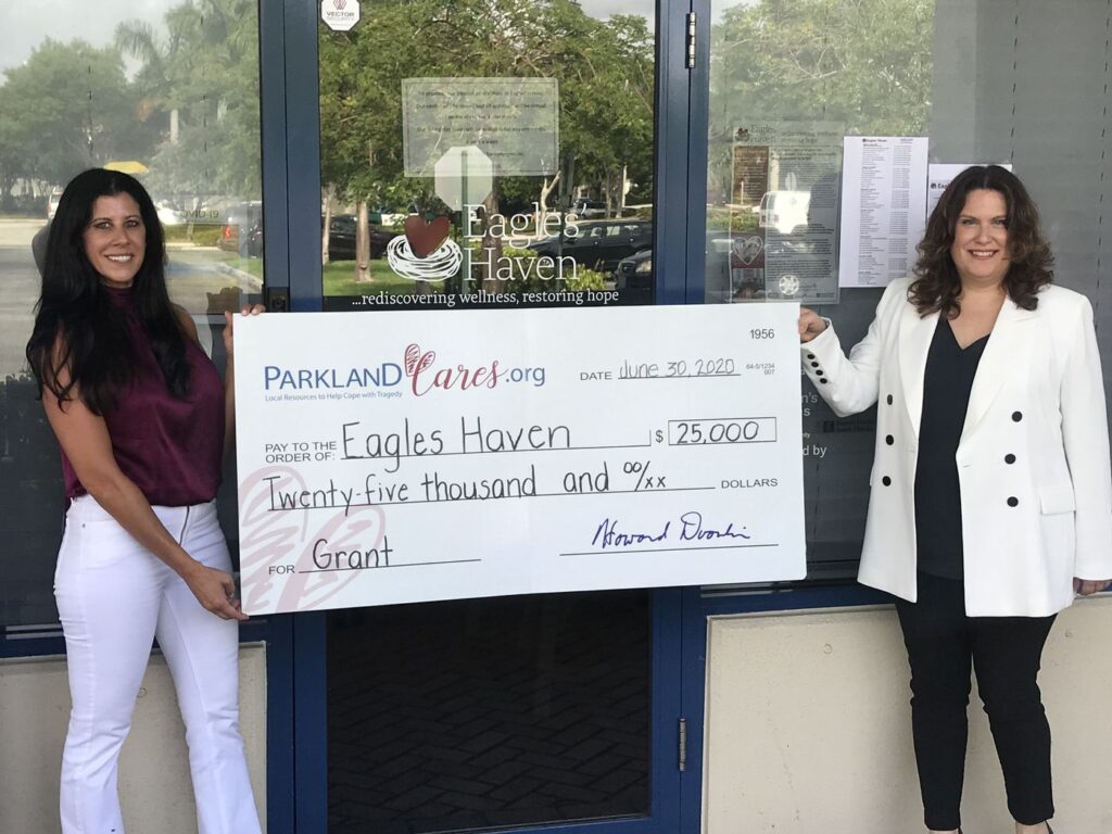 Two women hold an oversized Parkland Cares check for $25,000 made out to Eagles Haven, dated 30 June 2020, outside the Eagles’ Haven wellness center.