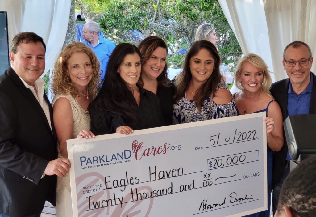 Seven supporters hold an oversized Parkland Cares check for $20,000 made out to Eagles Haven, dated May 2022, at an outdoor reception.