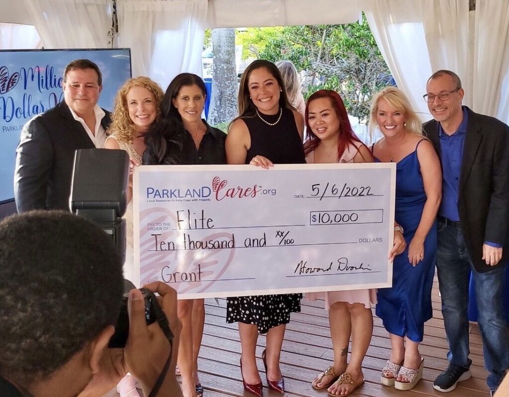 Seven supporters hold an oversized Parkland Cares check for $10,000 made out to FLITE, dated 6 May 2022, as a photographer takes the picture.