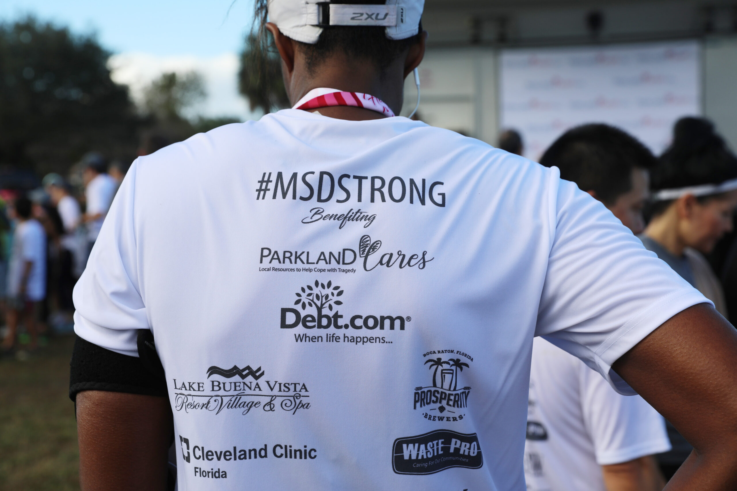 A runner photographed from behind wearing a #MSDSTRONG shirt benefiting Parkland Cares, printed with the logos of Debt.com, Lake Buena Vista Resort, Prosperity Brewers, Cleveland Clinic Florida and Waste Pro
